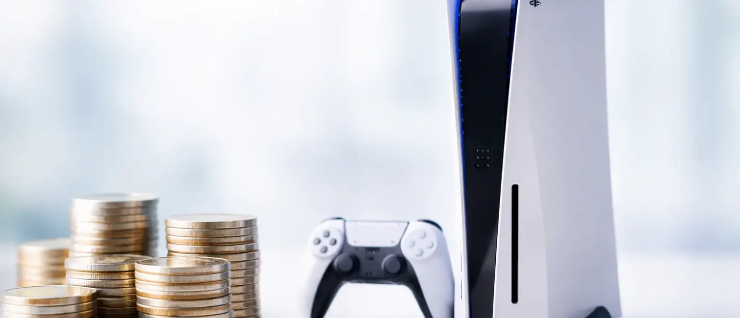 Minimalistisches Beitragsbild mit einer weißen Spielekonsole und Controller auf der rechten Bildseite sowie gestapelten Euromünzen im Vordergrund als Symbol für steigende Preise.